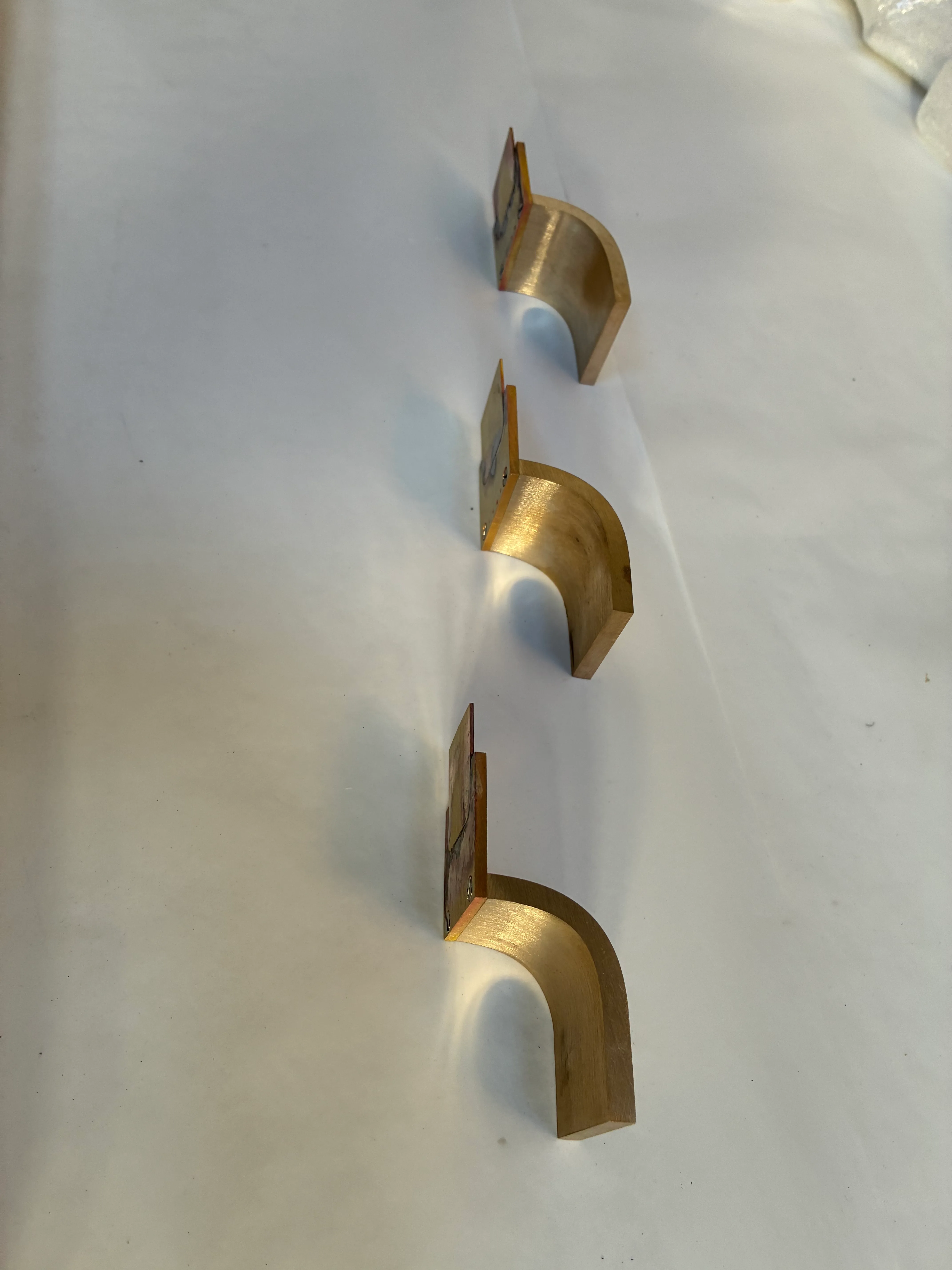 Pièces de fixation sur mesure en laiton massif pour poignée de douche Série de trois pièces de fixation ou poignées courbées en laiton massif alignées sur fond blanc