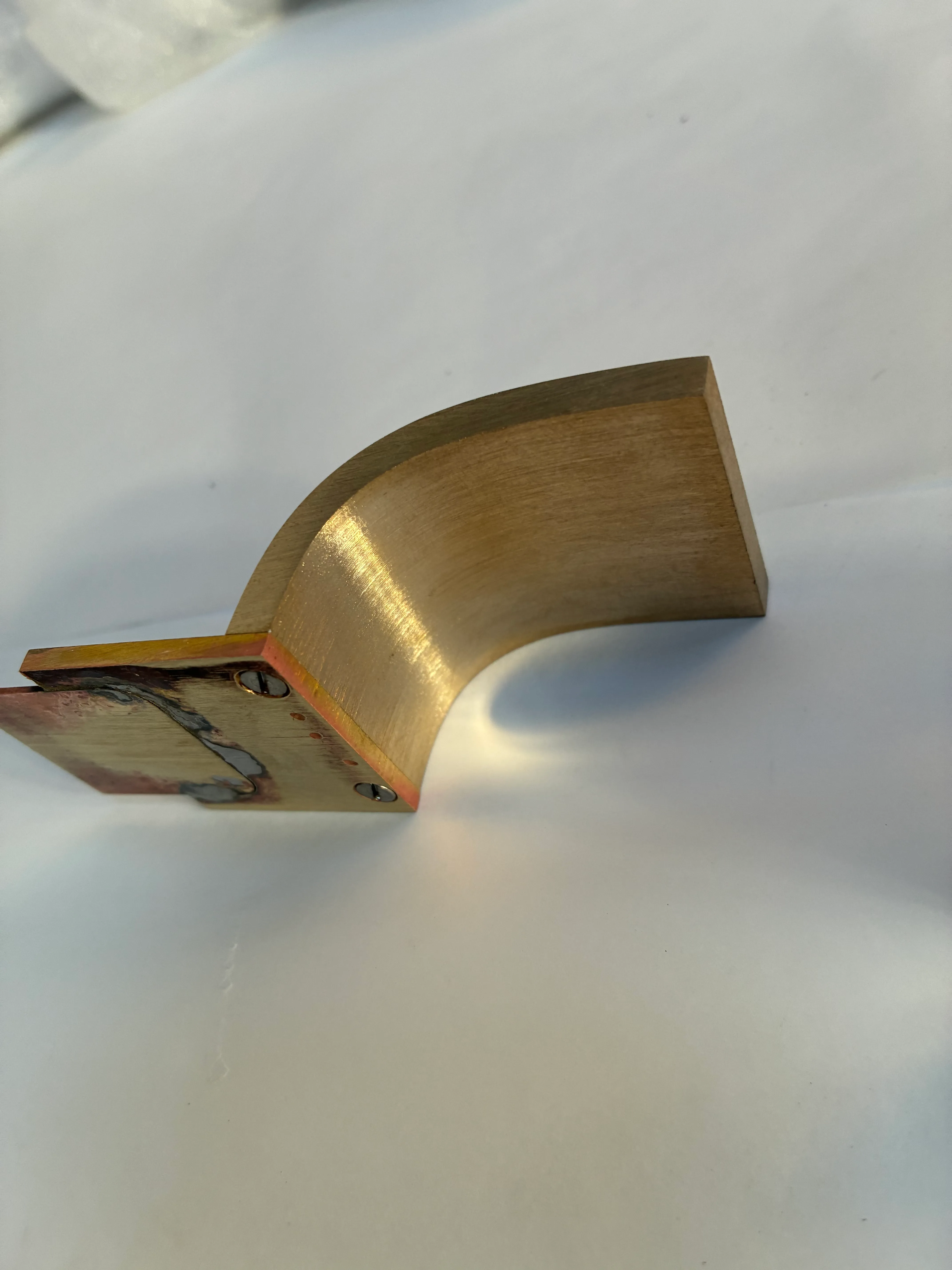 Détail de la platine de fixation d'une poignée de douche sur mesure en laiton Gros plan sur une pièce de fixation courbée en laiton massif, montrant la plaque de montage et les vis