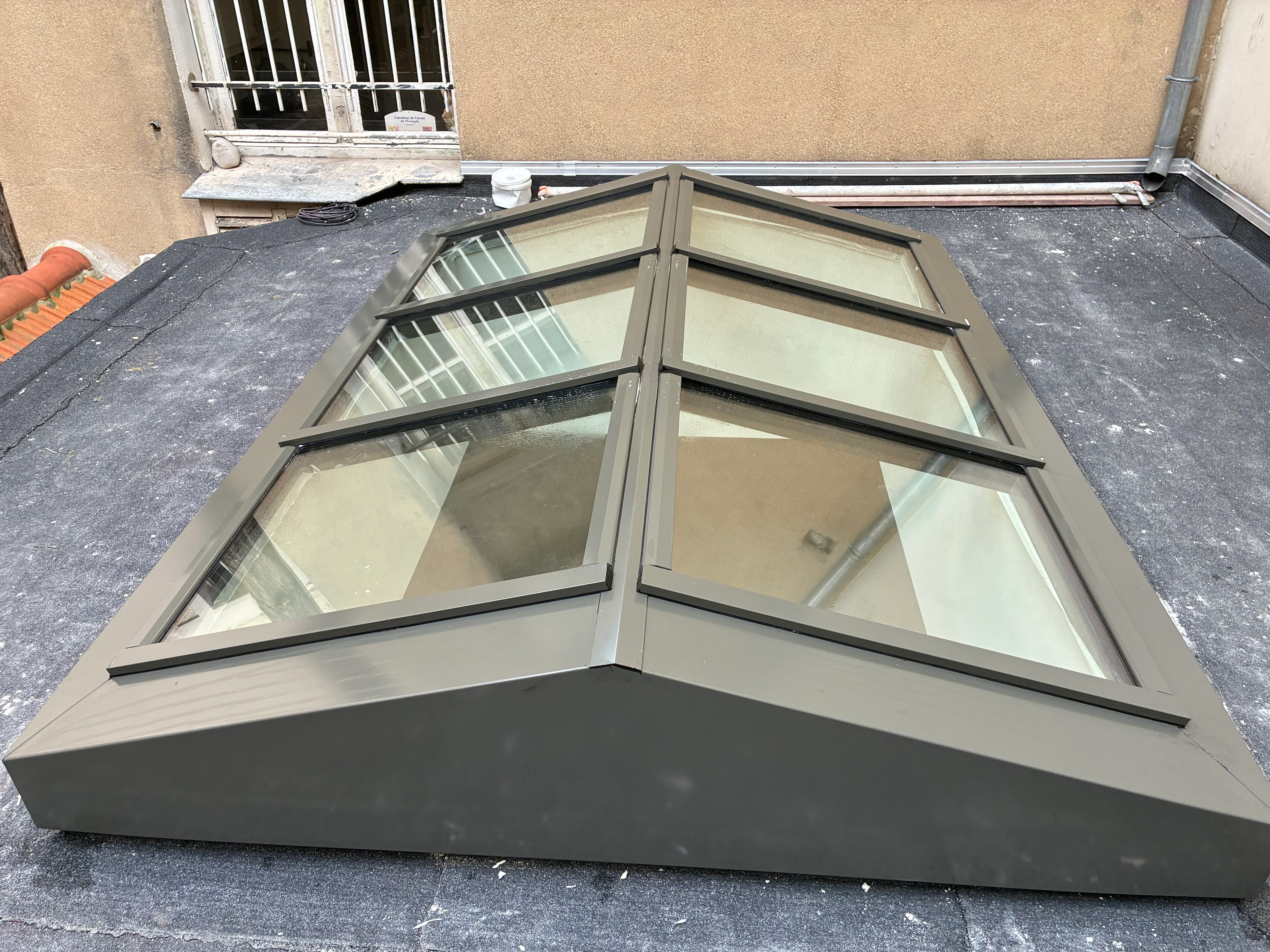 Structure acier à double pente pour verrière de toit sur mesure JANSEN Vue de profil d'une verrière de toit en acier thermolaqué gris anthracite, montrant sa structure angulaire à rupture de pont thermique posée sur une toiture plate.