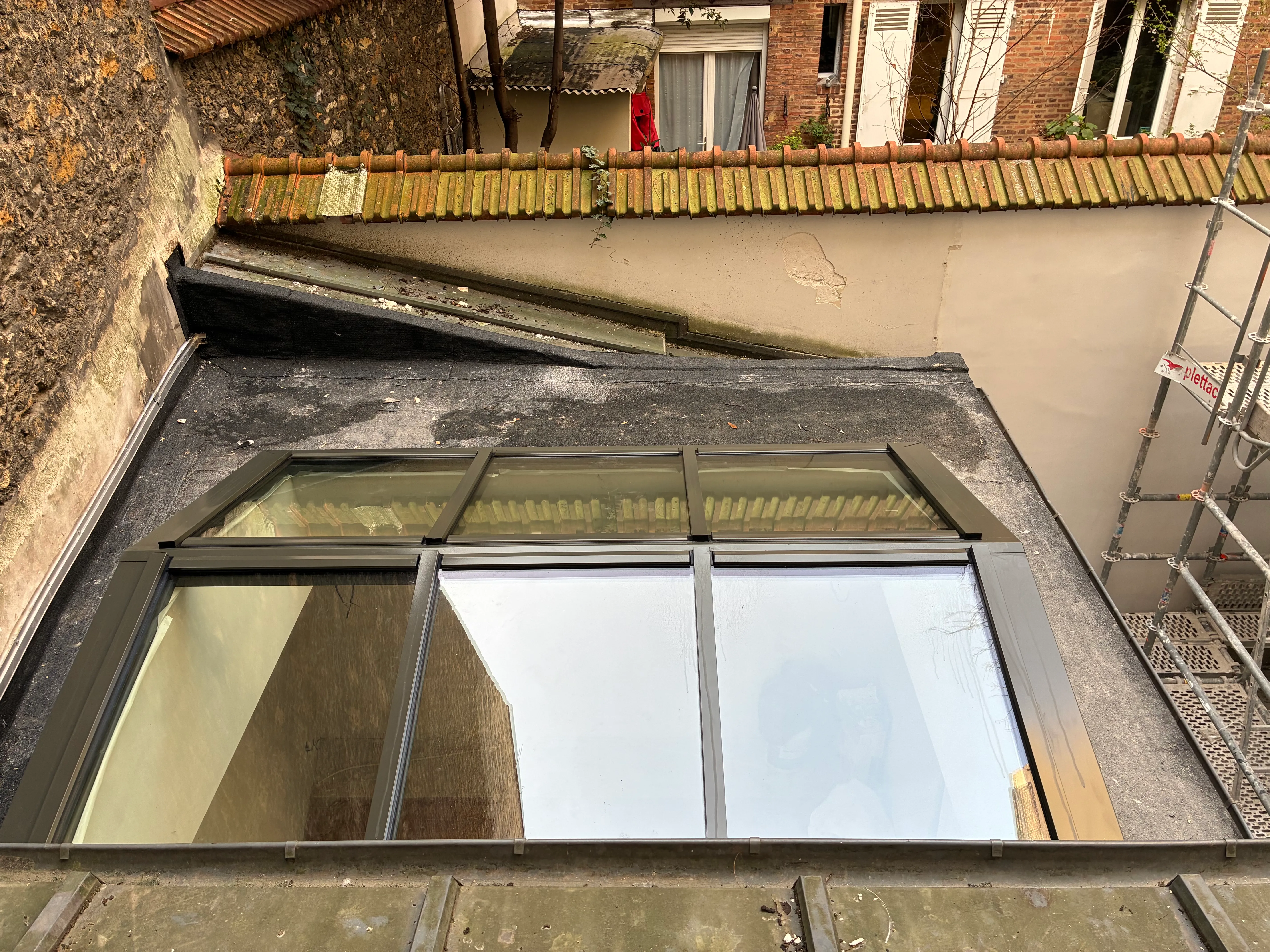 Installation d'une verrière en acier JANSEN sur un toit parisien Verrière de toit sur mesure vue de haut, avec un échafaudage métallique visible sur la droite et une façade parisienne traditionnelle en arrière-plan.