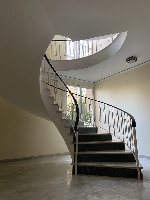 Réalisation d'une rampe d'escalier en ferronnerie d'art aux motifs géométriques Escalier tournant avec marches en pierre noire et une élégante rampe en ferronnerie blanche aux motifs géométriques