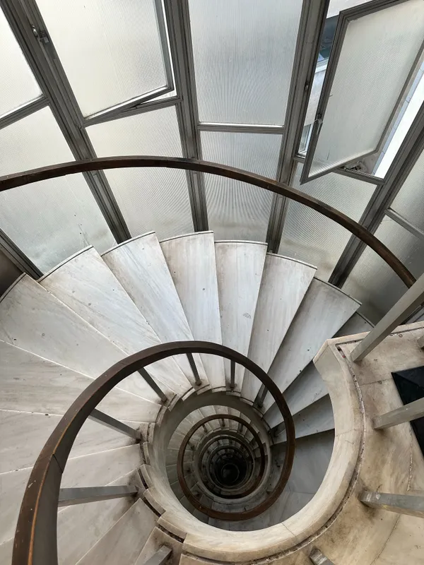 Restauration et intégration d'ouvrages métalliques dans des structures architecturales Vue plongeante vertigineuse sur un escalier en colimaçon en marbre blanc, bordé par une main courante continue