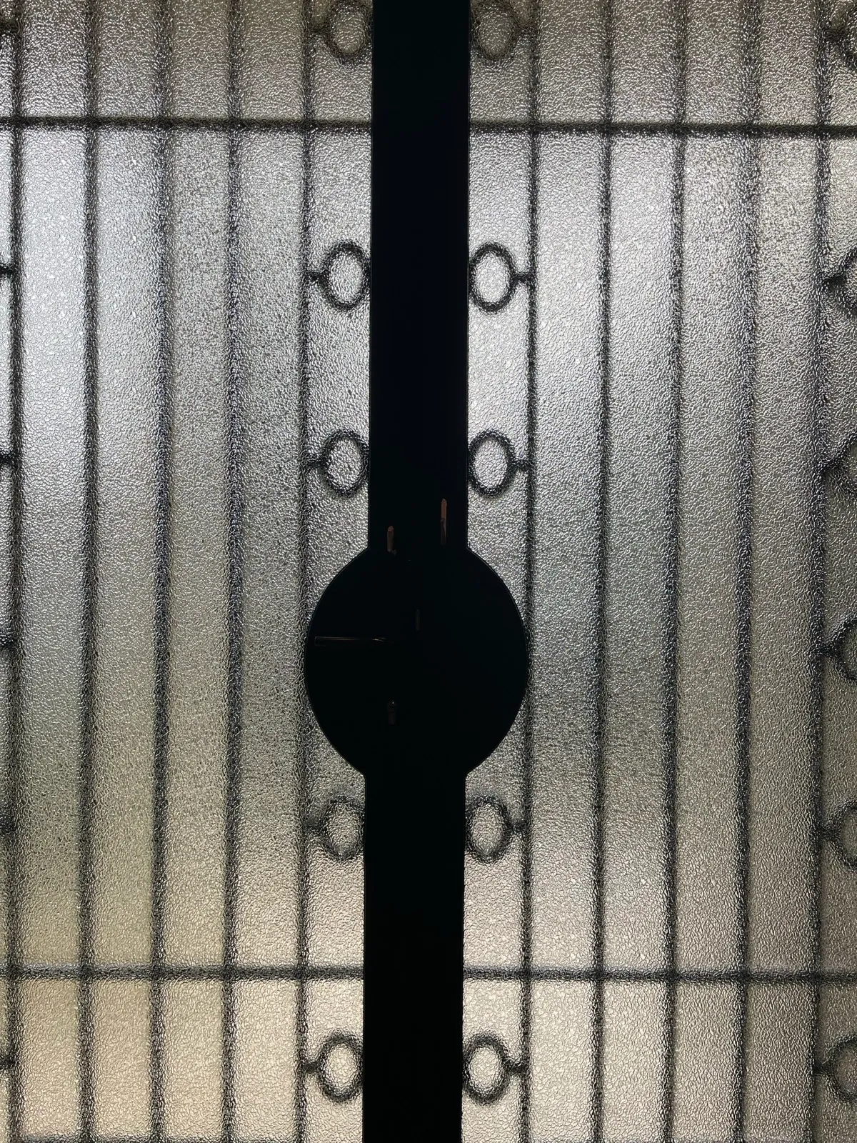 Restauration et travail de précision sur les serrures et mécanismes anciens Détail en gros plan d'une porte métallique vitrée, montrant le verre texturé rétroéclairé et la silhouette noire du mécanisme de serrure